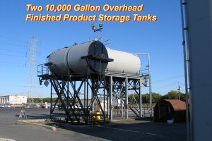 Large overhead sealcoat storage tanks at outdoor plant. Text on the photo says, "Two 10,000 gallon overhead finished product storage tanks."